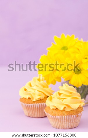 Cupcakes decorated with yellow cream and chrysanthemums on violet pastel background. Closeup photography of sweet baked dessert in minimalism concept.