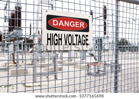 DANGER HIGH VOLTAGE sign on a metal electric fence around an electricity power station or plant, black letters on a white sign, no trespassing and entrance prohibited 