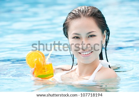 Smiling woman with cocktail swimming in pool