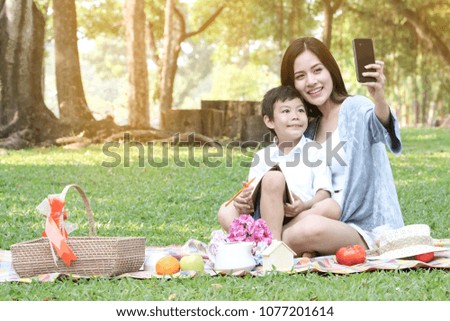 Family of mother and daughter son selfie take photo by camera of smartphone while a vacation picnic in a green grass park