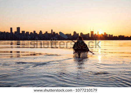 Adventurous girl on a sea kayak is kayaking during a vibrant sunny sunrise. Taken in Downtown Vancouver, British Columbia, Canada.