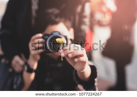 Young boy with mother taking photos of yellow flower on vacation in Cinematic color