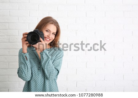 Female photographer with camera on brick background
