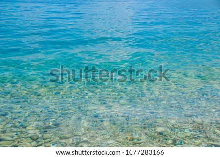 Transparent shallow water with rocky bottom, fading away to deeper area at top.Crystal clear water with transparent surface shine under the bright summer sun. Colorful underwater stones. Royalty-Free Stock Photo #1077283166