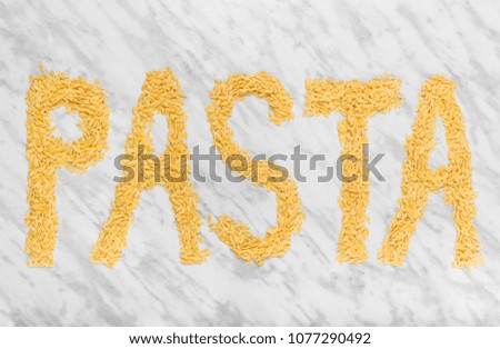 The word "PASTA" on marble background, written with rice-shaped tiny Orzo pasta.