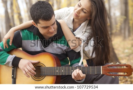 Romantic young couple embracing playing guitar outdoor in autumn sunlight