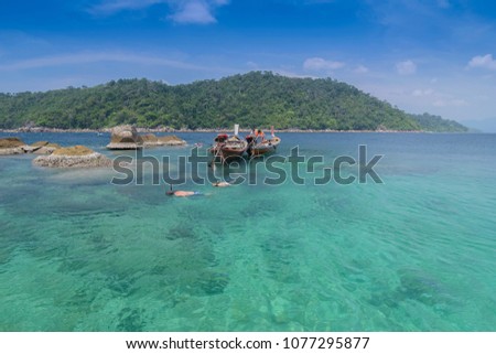 view of tourists snorkeling near by the arch rock looking for the small shark with long-tail boat floating in the blue-green sea and blue sky background, Ko Jabang, Satun, southern Thailand.