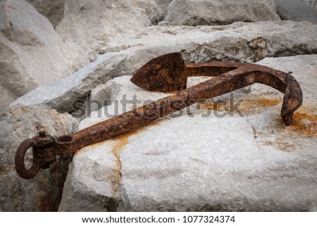 Small rusty anchor lying on rocks in a harbor, Croatia