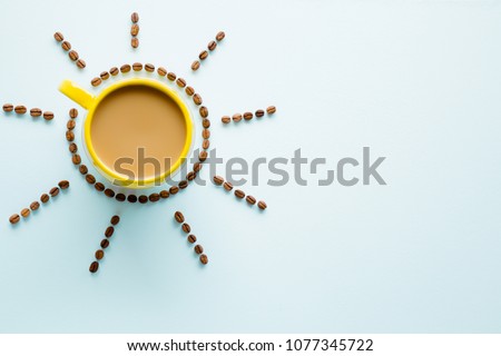 Yellow mug of coffee with milk on light pastel blue table from above. Wake up with morning coffee. Sun created from brown beans. Empty place for inspirational, motivational text or quote.  Top view. Royalty-Free Stock Photo #1077345722