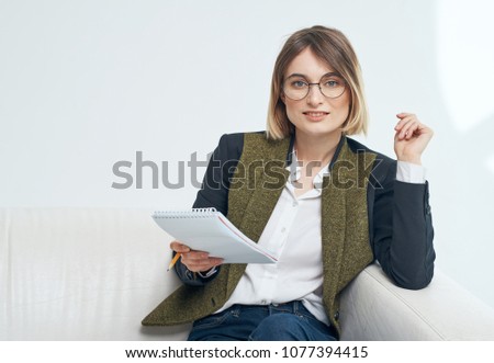   business woman wearing glasses in a jacket smiling sits on the sofa with documents, the place is free                             