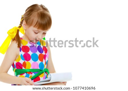 A beautiful Caucasian little blonde girl with long pigtails, in which large colored bows are braided, and a short bangs on her head. In a short summer dress.She reads the booklet.