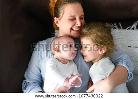 Picture of smiling young mother hugging two little children, closeup portrait of happy family, cute brunette female with daughter and son indoor