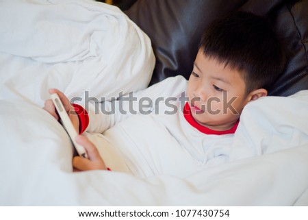 Asian Chinese boy playing smartphone on bed. watching smartphone. kid use phone and play game. child use mobile. addicted game and cartoon
