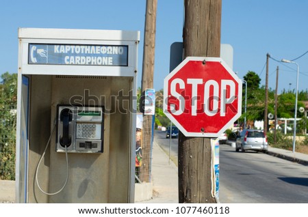 Road sign with Stop sign nailed to a wooden post next to the phone booth in Greece