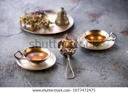 Herbal tea in metal cups and dried herbs on a gray concrete background