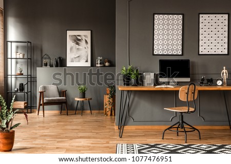 Patterned posters above desk with computer monitor in grey home office interior with plants Royalty-Free Stock Photo #1077476951