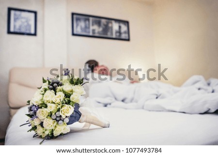 a wedding bouquet of white roses lay on a bed on the background of lovers in the room