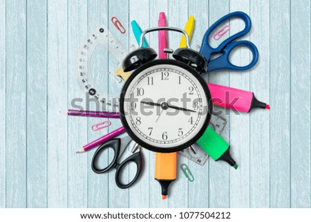 High angle view of school supplies under an alarm clock on the table