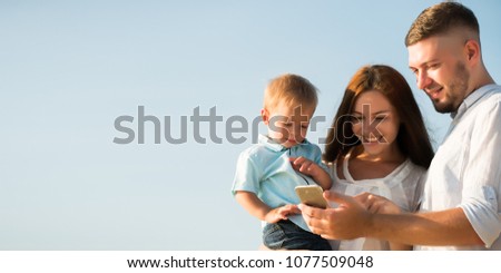 Happy Family are look at mobile phone and hug on the beach While relaxing on weekends with blur sea background in travel and holiday concept