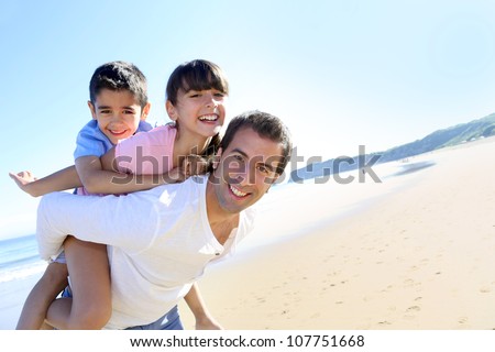 Daddy carrying children on his back at the beach Royalty-Free Stock Photo #107751668