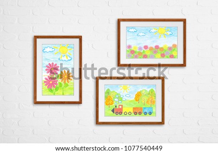 Three frames with colored pencils drawings on white bricks wall. Colorful flowers and  butterflies, toy train in the field. Kid's art interior decor. 