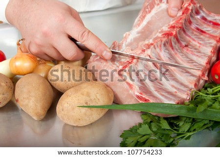 cook hands cutting raw meat at kitchen table