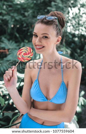 smiling beautiful girl in bikini posing with lollipop on tropical resort