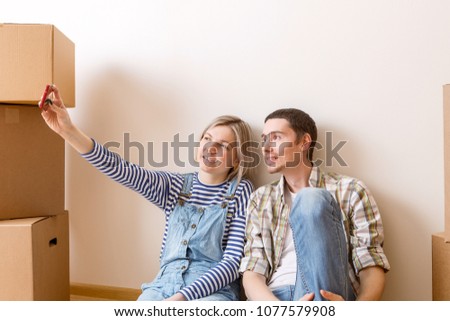 Photo of young married couple doing selfie sitting on floor among cardboard boxes