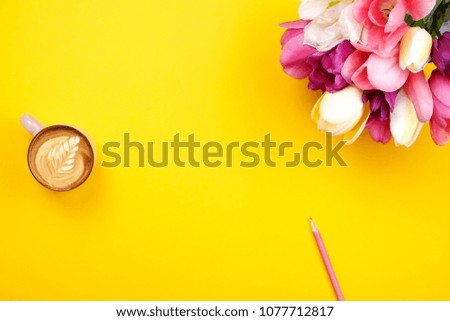 Feminine desktop composition with blank sheet notebook, pencil, coffee cup, tulips bouquet on yellow background. Girlie workplace, flowers for mother's day. Top view, flat lay, close up, copy space.