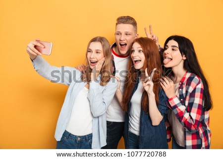 Group of cheerful school friends taking a selfie while having fun together over yellow background