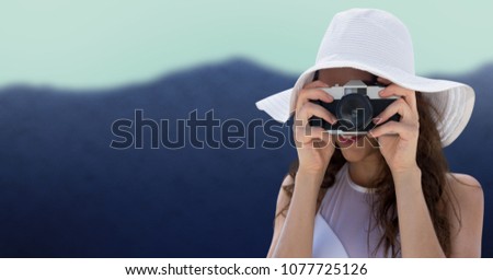Close up of millennial woman in summer hat with camera against blurry mountain