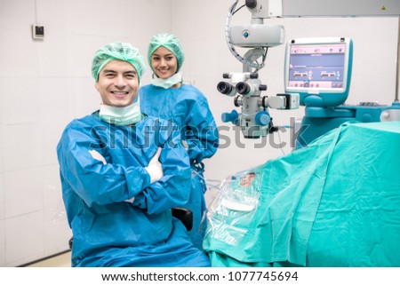 Eye surgeon at work. Young caucacian male surgeon with his beautiful chinese assistant woman with senior patient portrait. Real operating theater room. Medical concept.