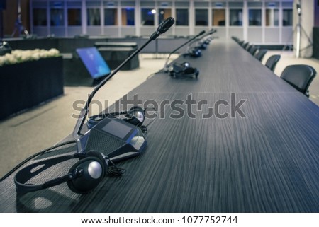 A row of microphone and headphone sets for speech and translation on a business or congress meeting on a desk. Translation booths are seen in the background.