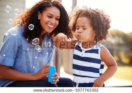 Young mixed race mother and daughter blowing bubbles outside Royalty-Free Stock Photo #1077765302
