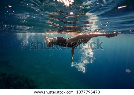 Professional female swimmer swim in the ocean on the sunrise, underwater picture