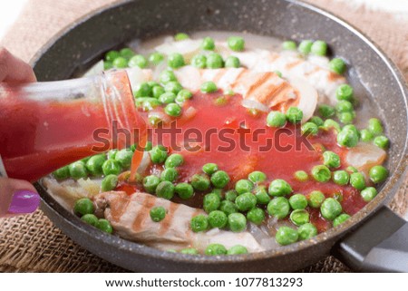 Chicken fillet, onion, peas and tomato sauce in a frying pan
