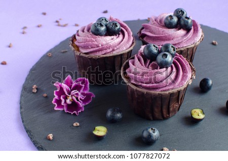 Cupcakes with blueberry creme on black plate on purple background