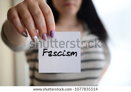 Young sad girl shows a white sticker. Caucasian brunette holding a sheet of paper with message. Fascism