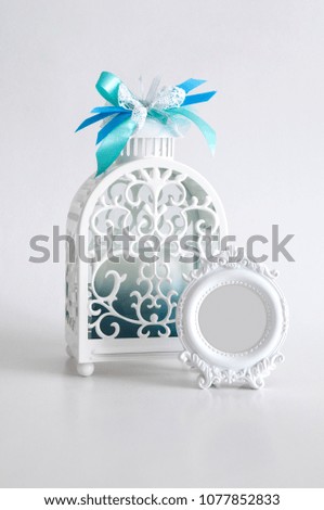 Beautiful white lantern with a candle inside and a round vintage photo frame on white background. Home decor. Clipping path inside the frame