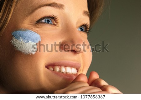 Portrait of a woman with the flag of the Argentina painted on her face. Young female caucasian model closeup. Football, soccer, fan concept. Human emotions, facial expressions concepts
