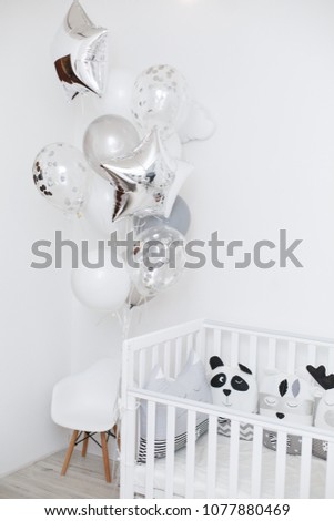 White interior of child room. Child bed and balloons in white room. Birthday party for baby. Kinder room. Stylish kid room with decorative pillows for care in a bed