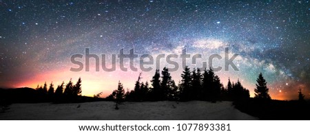 The dark mountain night shines with millions of stars over the fabulous Alpine peak in the Carpathians, the Milky Way of the Galaxy passes over a coniferous forest with a huge arc