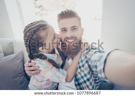 Sweet lovely schoolgirl with pigtails kissing with pout lips her father with red hair in cheek who shooting self portrait on front camera, trust idyllic understanding support concept