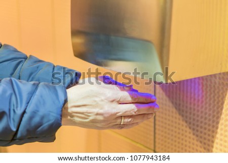 female hands in blue coat under hand dryer in public toilet room