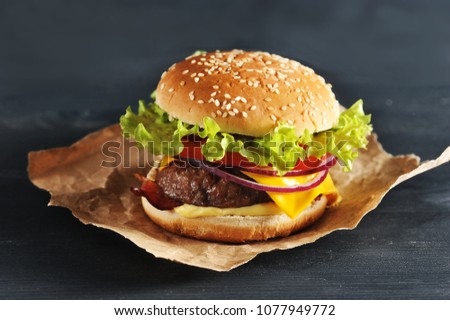hamburger with onion tomato and salad on Kraft paper on dark wooden background - side view