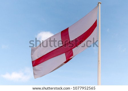 national flag of England St Georges flag blowing in the wind with blue sky in background