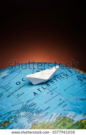 Paper boat crossing the Atlantic Ocean on a globe with sunrise light on the background