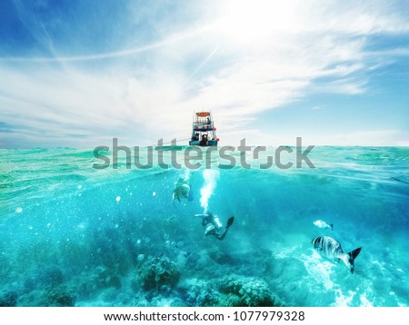 Scuba divers underwater and fishing tour boat above the Caribbean Sea in Cozumel, Mexico Royalty-Free Stock Photo #1077979328