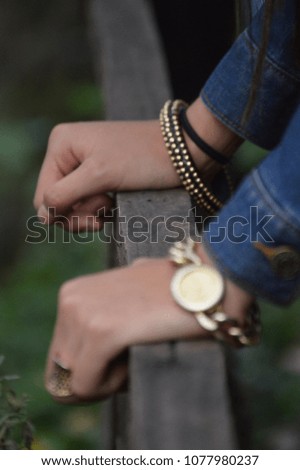 Vertical photograph of two hands over an old dark wood fence with golden jewelry