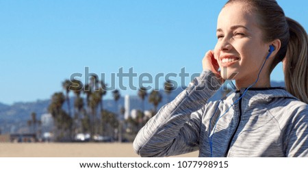 fitness, sport and technology concept - close up of happy woman listening to music in earphones over venice beach background in california